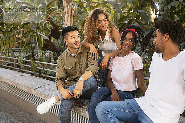 Smiling multiracial friends spending leisure time on wall
