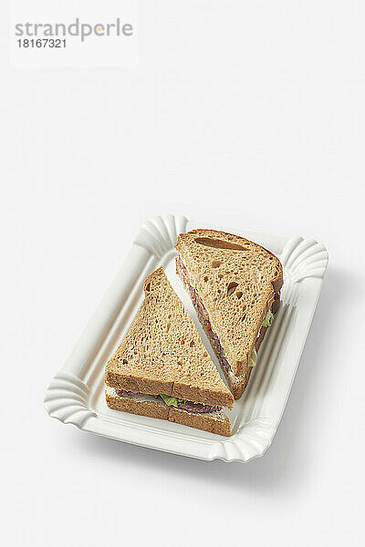 Schwarzbrot-Schinken-Sandwich auf Tablett vor weißem Hintergrund