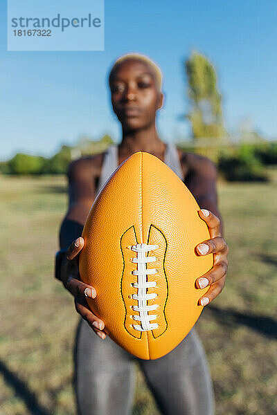 Junger Sportler zeigt American Football an einem sonnigen Tag