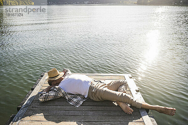 Mature man with hat on face resting on jetty