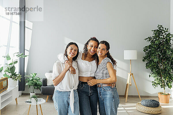 Smiling multiracial friends with arms around at home