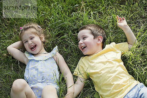 Cheerful cute siblings relaxing on grass at park