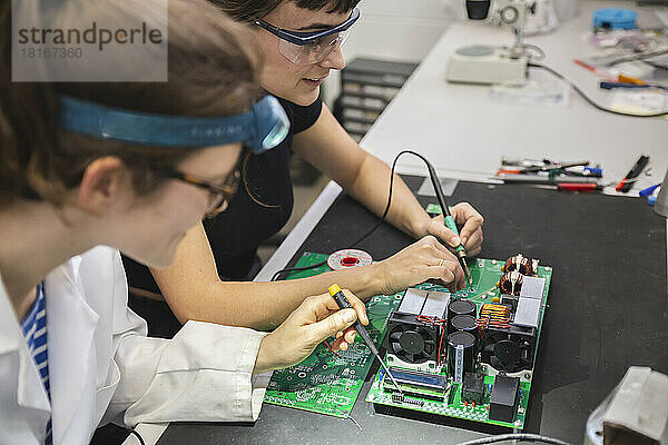 Technikerinnen löten Motherboard auf Tisch in Werkstatt