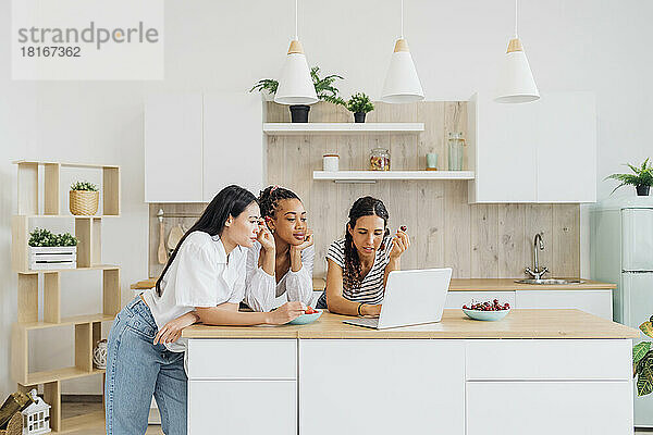 Flatmates leaning on kitchen counter sharing laptop at home