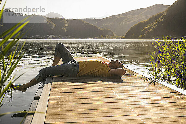 Mature man relaxing on jetty over lake by mountains