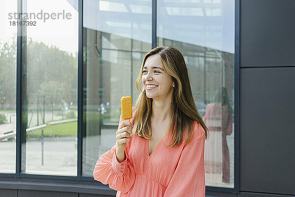 Lächelnde Frau hält Eis vor einer Glaswand