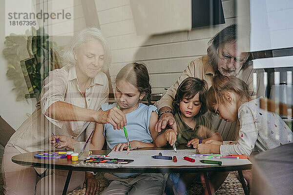 Großeltern mit Kindern malen zu Hause  gesehen durch Fensterglas