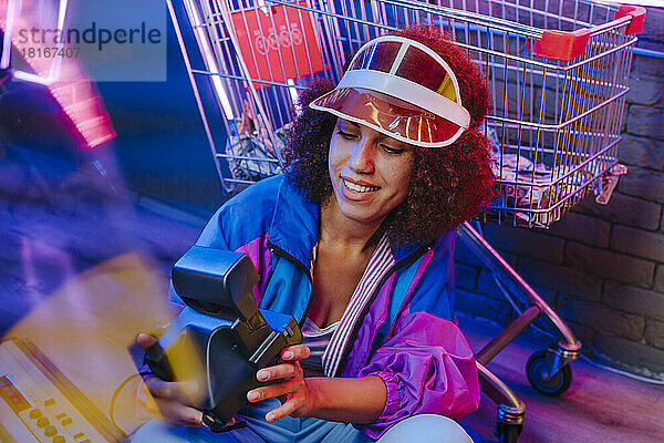Lächelnde Frau hält Sofortbildkamera vor Einkaufswagen
