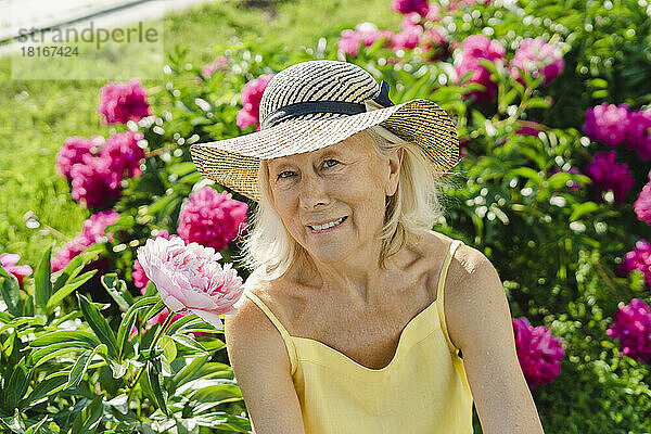 Ältere Frau mit Hut inmitten einer Blume im Garten