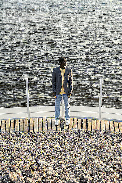Junger Geschäftsmann steht auf der Promenade vor dem Meer