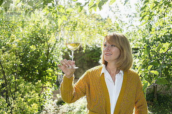 Lächelnde reife Frau hält ein weißes Glas Wein im Garten