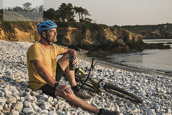 Nachdenklicher reifer Mann sitzt mit Fahrrad auf Kieselsteinen