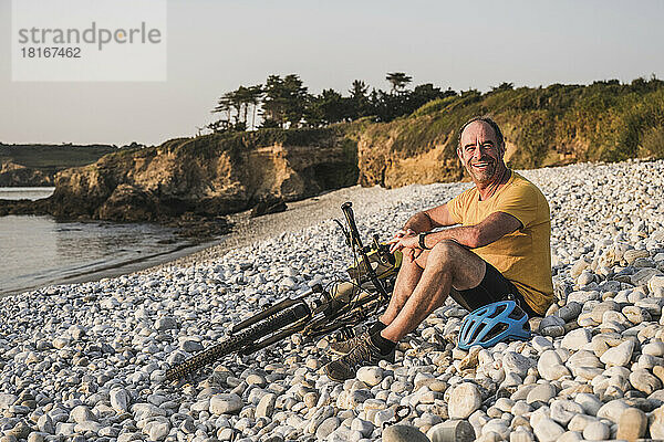 Glücklicher reifer Mann sitzt mit Fahrrad am Strand