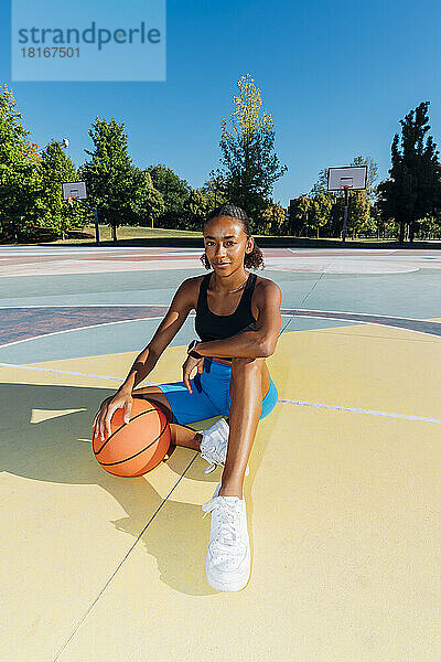 Junger Basketballspieler mit Ball sitzt auf dem Platz