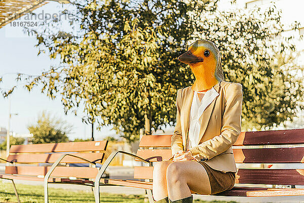 Freiberufler mit Vogelmaske sitzt auf Bank im Park