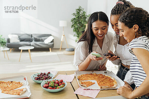 Lächelnde Freunde  die Smartphones in der Küche benutzen