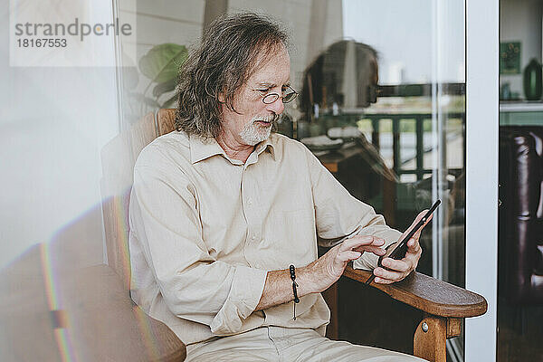 Älterer Mann sitzt zu Hause auf einem Stuhl und benutzt einen Tablet-PC