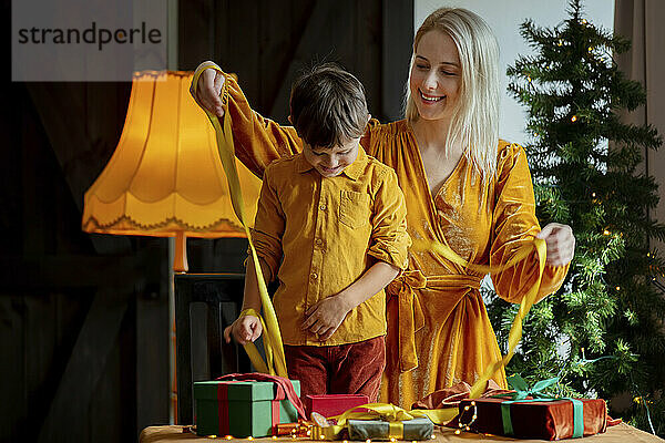 Glückliche Mutter mit Sohn  die zu Hause Geschenke mit Schleife verpackt