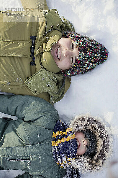 Glückliche Frau mit Sohn  der auf Schnee liegt