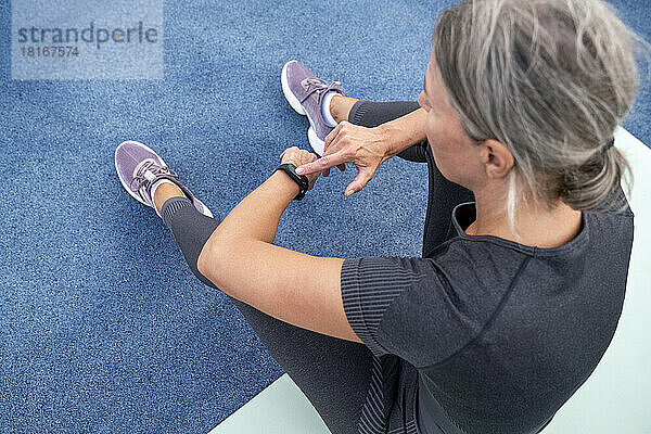 Mature woman checking time in smart watch sitting on exercise mat