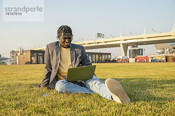 Lächelnder Geschäftsmann mit Laptop im Gras sitzend