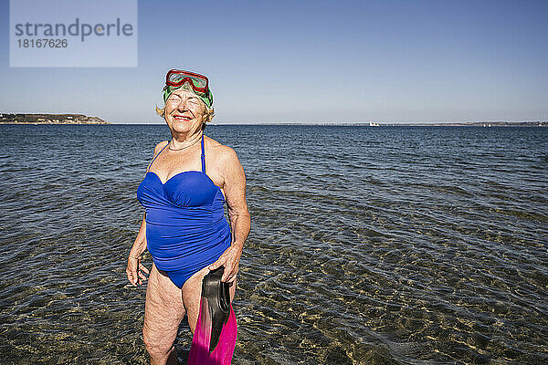 Lächelnde Frau mit Tauchflossen  die im Meer steht