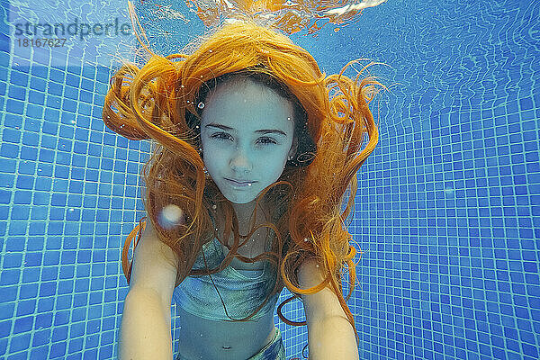 Rothaariges Mädchen in Badebekleidung schwimmt unter Wasser