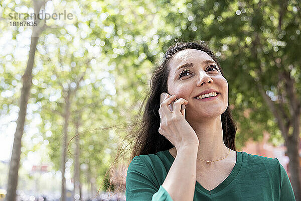 Glückliche Frau  die vor einem Baum mit ihrem Smartphone spricht