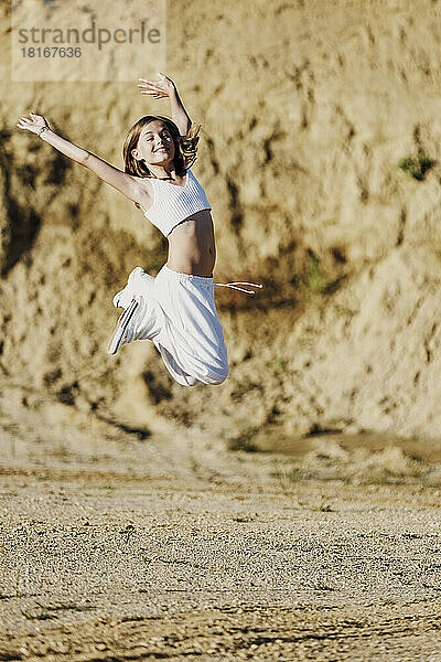 Fröhliches Mädchen springt an einem sonnigen Tag vor Sanddünen