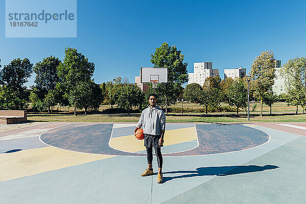 Junger Sportler mit Basketball auf dem Sportplatz an einem sonnigen Tag