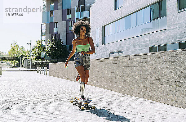 Junge Frau läuft an einem sonnigen Tag vor dem Gebäude Longboard