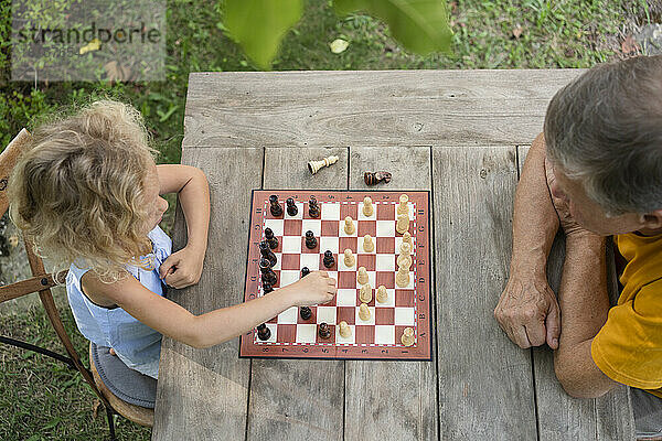 Granddaughter and grandfather playing chessboard in garden