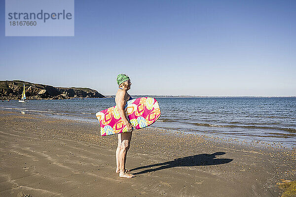Nachdenkliche Frau mit Surfbrett und Blick aufs Meer
