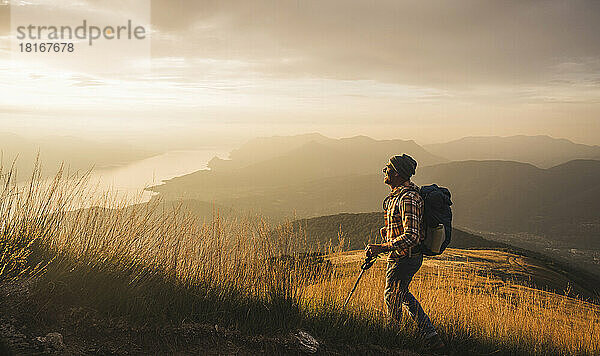 Mann mit Wanderstock und Rucksack wandert bei Sonnenaufgang