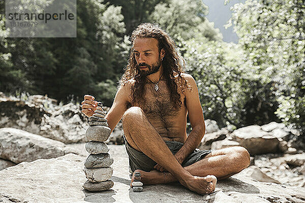 Nackter Oberkörper junger Hipster stapelt Steine ??auf einem Felsen