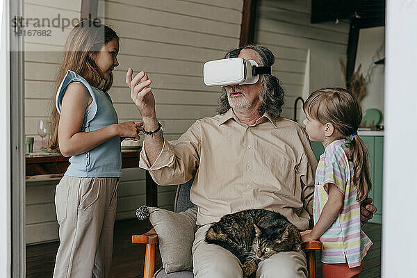 Großvater trägt Virtual-Reality-Simulator und gestikuliert mit Enkelkindern zu Hause