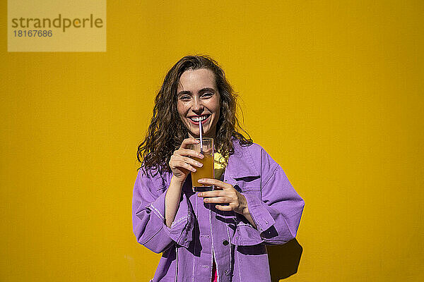 Glückliche Frau trinkt Orangensaft vor der Wand