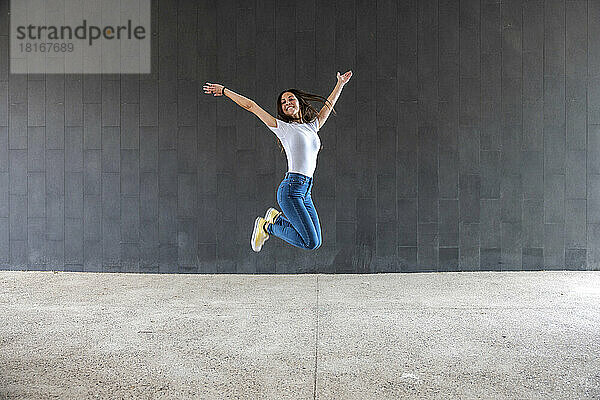 Glückliche Frau springt auf Fußweg vor grauer Wand