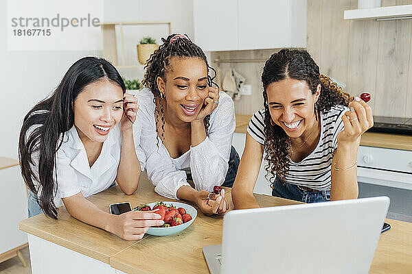 Fröhliche Freunde  die Früchte essen und zu Hause Videoanrufe auf dem Laptop machen
