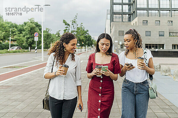 Junge Frau teilt Smartphone mit Freunden und geht auf Fußweg
