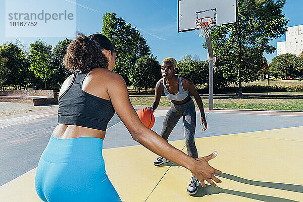 Junge Sportlerin dribbelt Basketball und spielt mit einem Freund auf dem Sportplatz