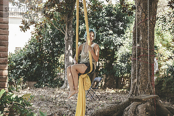 Frau hängt an Luftseide und praktiziert Acroyoga am Baum