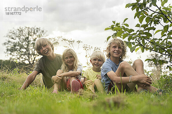 Lächelnde Brüder und Schwestern mit blonden Haaren sitzen im Gras