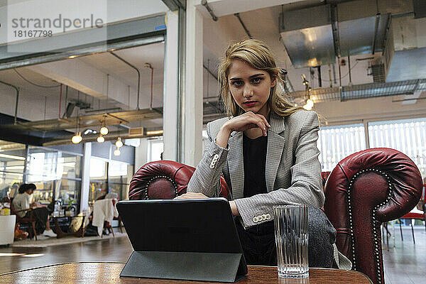 Junge Frau sitzt im Sessel und arbeitet an einem digitalen Tablet