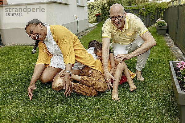Glückliche Eltern mit Kindern  die im Garten auf dem Rasen spielen