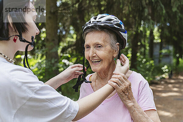 Urenkelin hilft Seniorin mit Fahrradhelm im Park