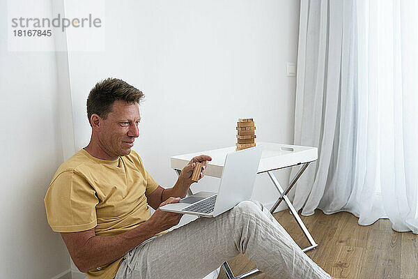 Lächelnder reifer Mann zeigt Spielzeugblock bei Videoanruf über Laptop zu Hause