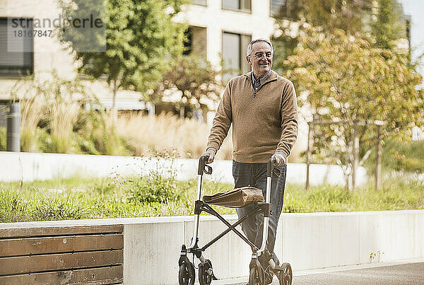 Lächelnder älterer Mann mit Gehhilfe  der auf dem Fußweg läuft