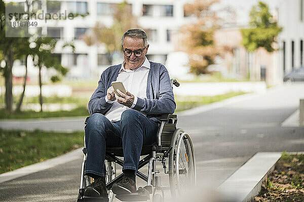 Lächelnder älterer Mann mit Smartphone im Rollstuhl