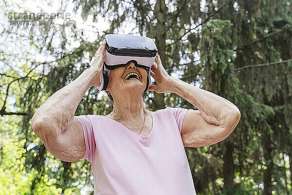 Glückliche ältere Frau schaut durch VR-Brille im Park zu